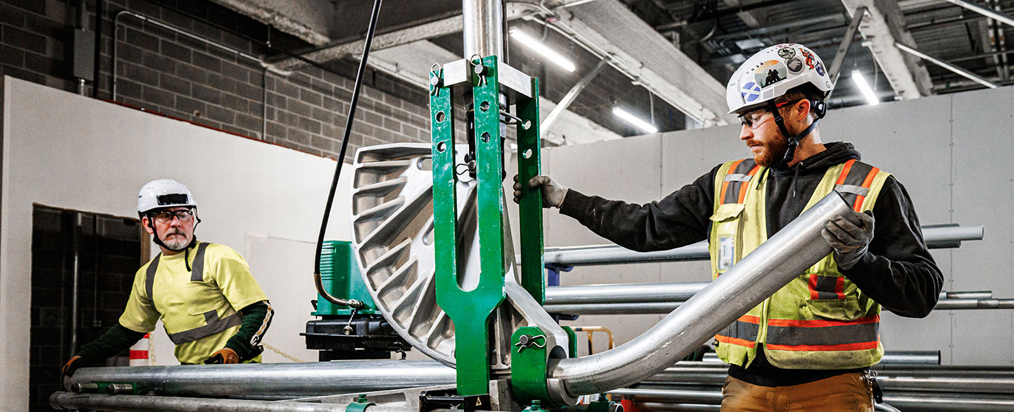 Two electrical contractors positioning a metal pipe into a machine